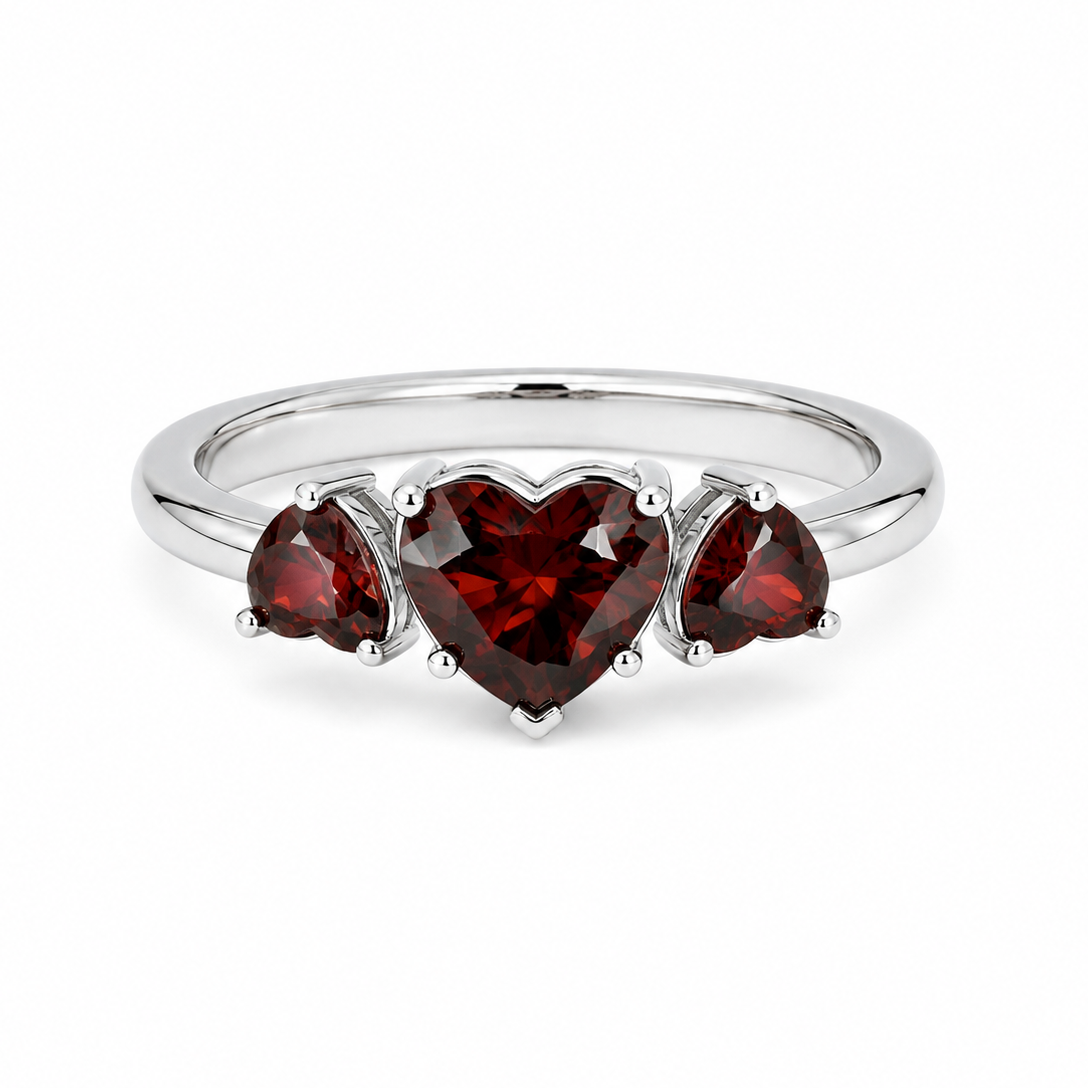 A silver ring featuring three heart-shaped dark red gemstones, with a larger central heart and two smaller side hearts, set on a plain white background.

